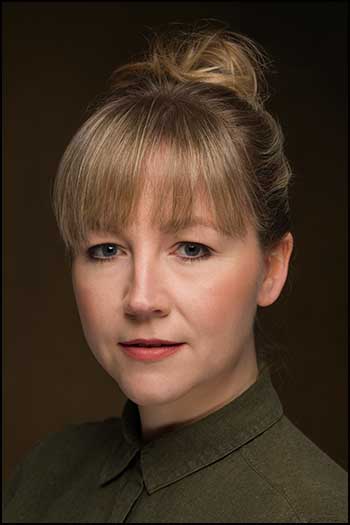 Headshot photograph hair up geen shirt, brown background.